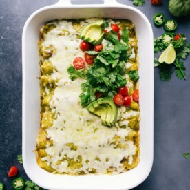 Warm and flavor packed green chile chicken enchiladas in the pan, topped with fresh herbs and tomatoes.