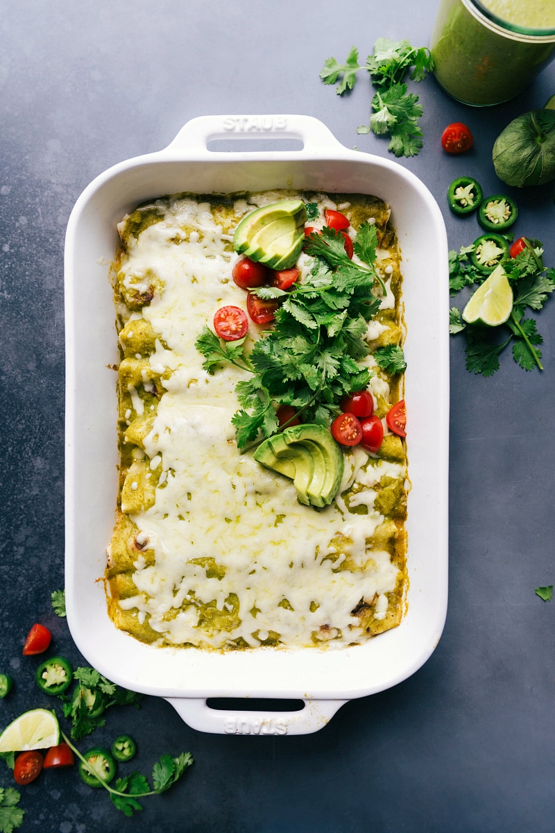 Warm and flavor packed green chile chicken enchiladas in the pan, topped with fresh herbs and tomatoes.