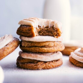 Stacked pumpkin cinnamon roll cookies with a bite taken out of the top one, revealing their fluffy interior and delightful frosting.