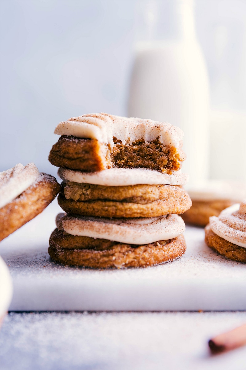 Stacked pumpkin cinnamon roll cookies with a bite taken out of the top one, revealing their fluffy interior and delightful frosting.