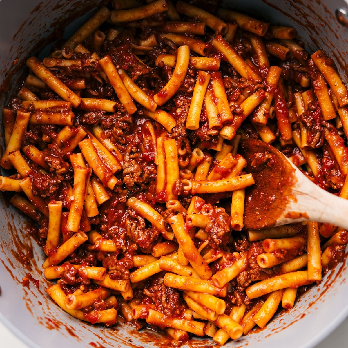 Pasta Being Combined With The Meat Sauce Cooked pasta being tossed with the rich meat sauce.