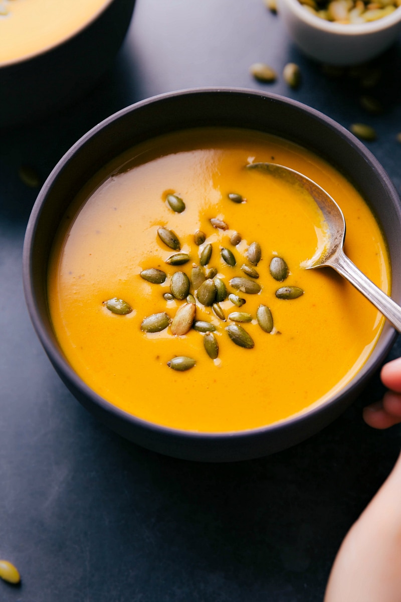 Up-close overhead image of Carrot Soup in a bowl with someone taking a spoonful out of it.