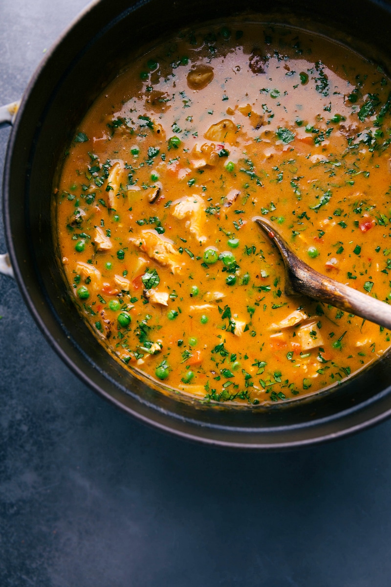 Rich and aromatic chicken and curry soup being stirred with a wooden spoon, showcasing vibrant colors and hearty ingredients.