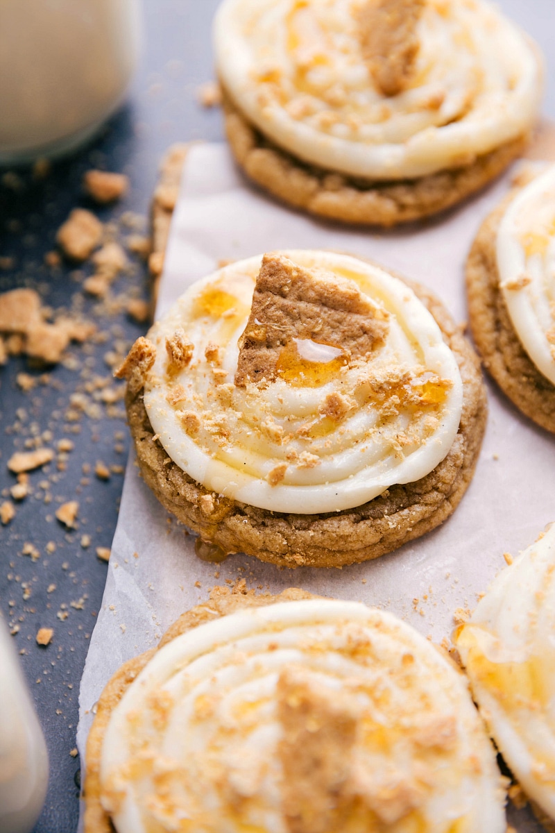 Frosted honey graham cookies topped with creamy frosting, garnished with graham cracker crumbs, a drizzle of honey, and a large graham cracker piece.