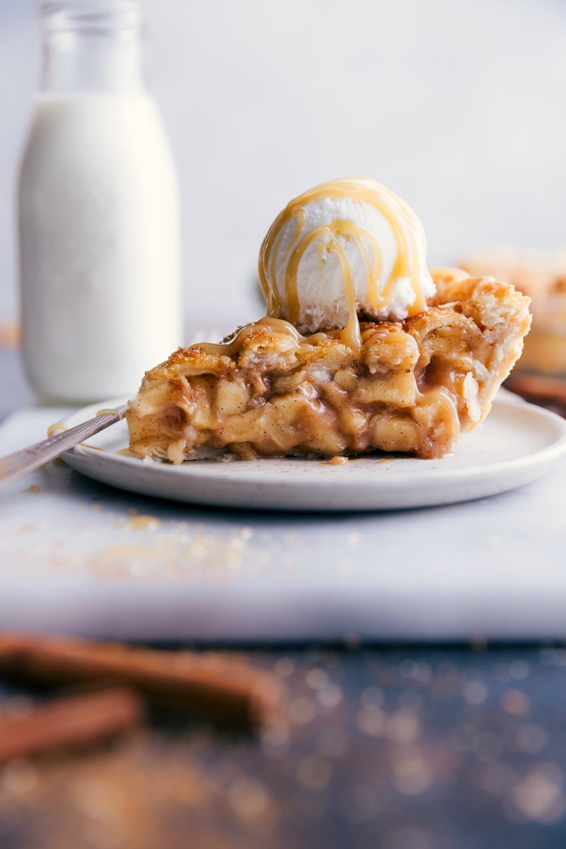 Image of a slice of apple pie with ice cream and caramel sauce on top.