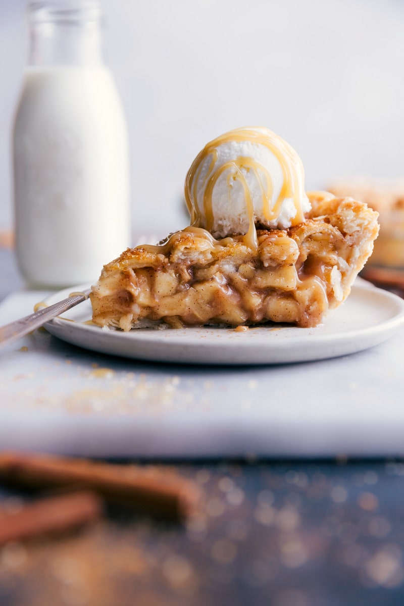 Slice of apple pie with ice cream and caramel sauce on top.