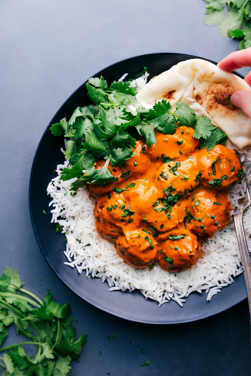 View of a plate with Butter Chicken Meatballs on a bed of rice, garnished with cilantro and naan bread on the side.