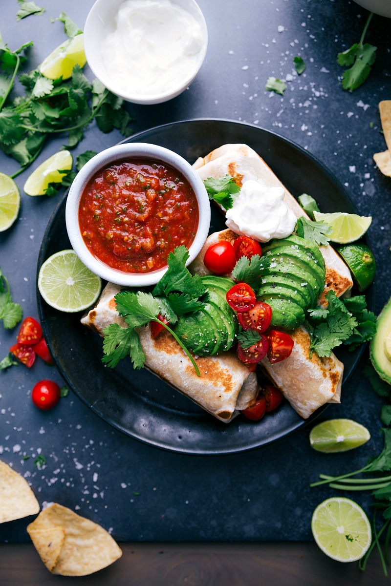 Healthy burritos garnished with avocados, tomatoes, fresh herbs, and sour cream ready to be enjoyed.