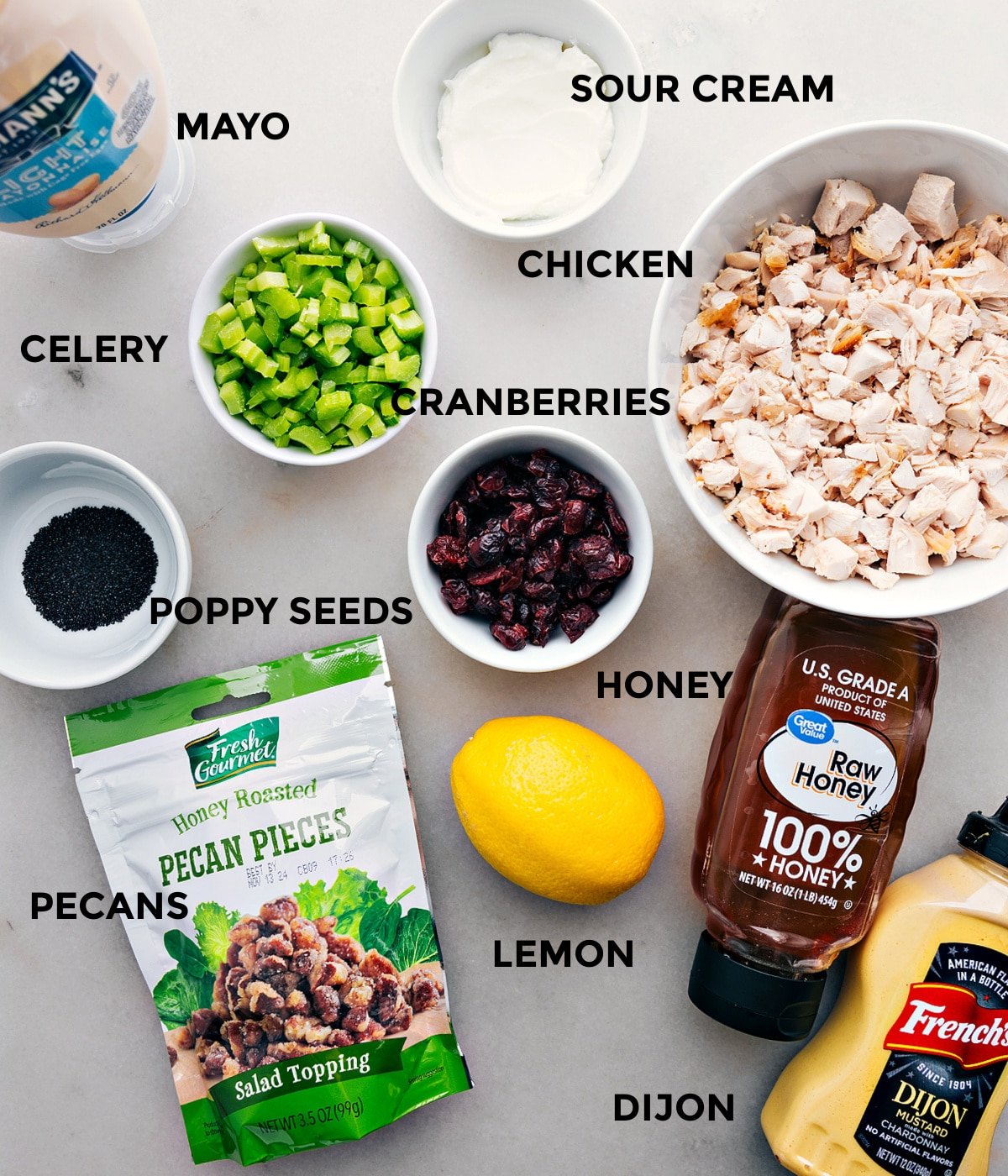 All the ingredients in this recipe including meat, sour cream, mayo, celery, cranberries, poppy seeds, lemon, dijon, pecans, and honey prepped out for easy assembly.