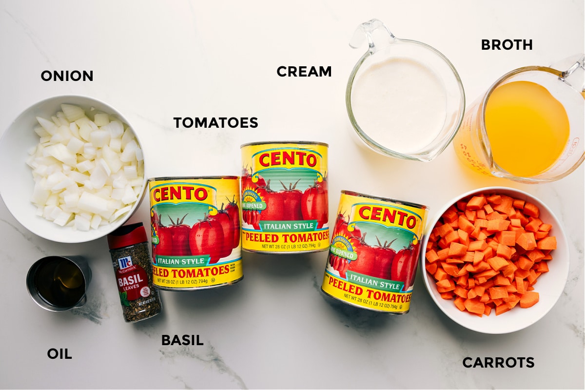 All the ingredients in this recipe prepped out for easy assembly including the onion, oil, basil, tomatoes, cream, broth, and carrots.
