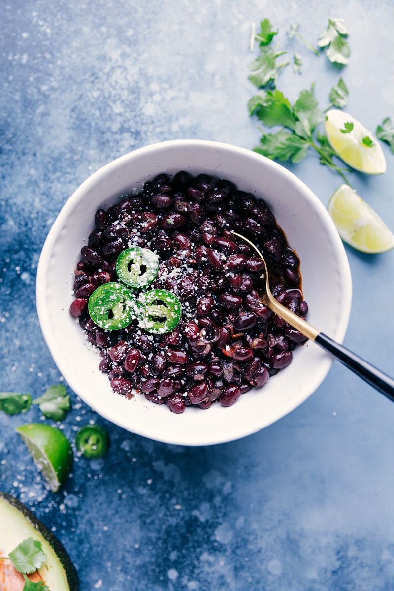 Overhead view of a bowl of Black Beans, with cilantro, lime and sliced jalapeño on the side.