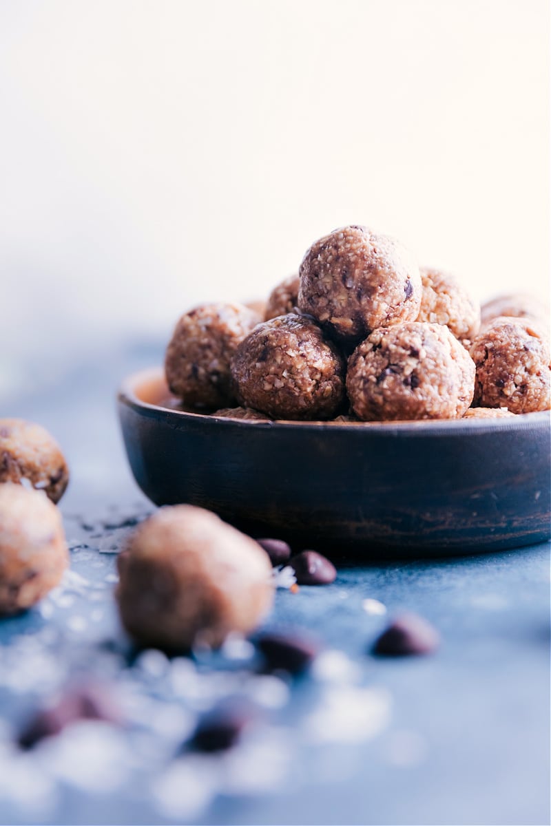 Simple seven-ingredient Oatmeal Energy Balls are filled with oats, coconut, and chunks of chocolate. These delicious pop-able bites taste like healthy oatmeal chocolate chip cookies! Recipe via ChelseasMessyApron.com #oatmeal #energyballs #healthy #peanutbutter #honey #coconut Image showing a bowl of Oatmeal Energy Balls.