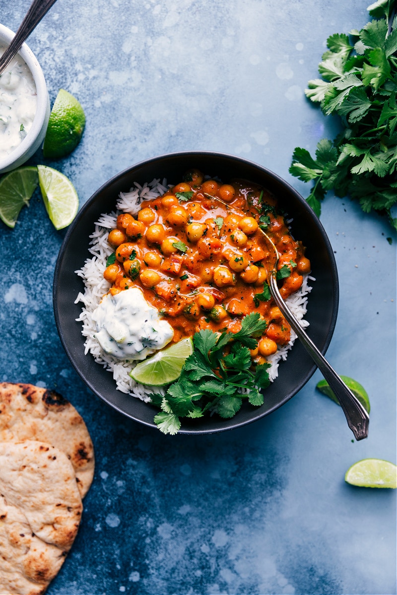 Overhead view of Chickpea Curry, served with rice, cilantro, naan bread and coconut raita.