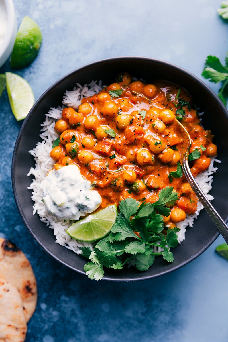 Overhead view of Chickpea Curry with basmati rice, raita, lime and cilantro.