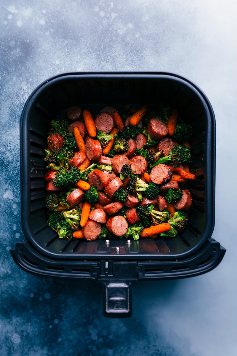 Overhead view of the sausage and veggies in the air fryer basket.