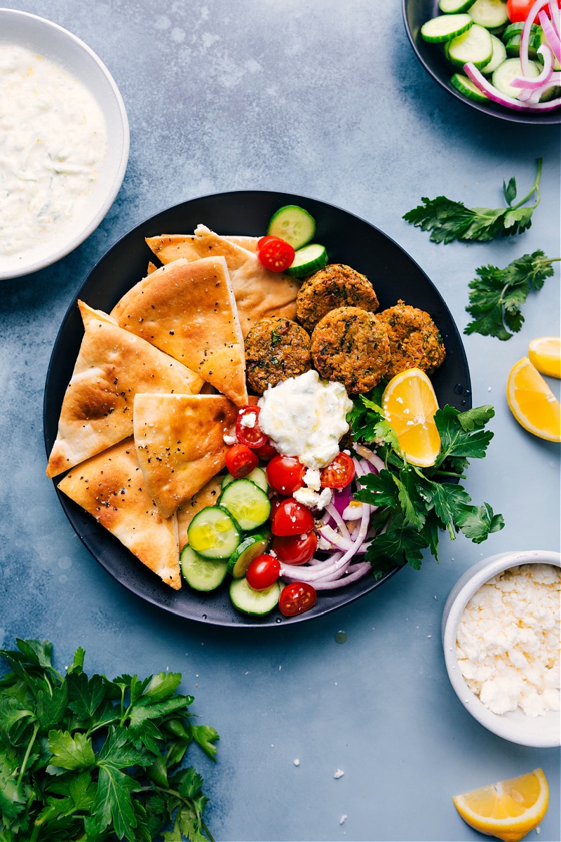The traditional fried falafel patties are getting a makeover today in the Air Fryer! Air Fryer Falafel is made with good-for-you, nourishing ingredients and is loaded with flavor. Serve with some air fryer pita, a quick tzatziki sauce, and fresh veggies for a delicious, healthful vegetarian meal that is high in protein. Recipe via chelseasmessyapron #dinner #quick #easy #simple #vegetarian #tzatziki #sauce #pita #airfryer #falafels A plate filled with Air Fry Falafels, pita triangles, and tzatziki sauce
