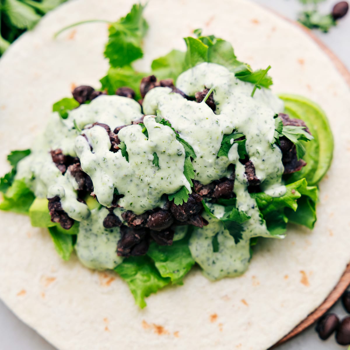A black bean wrap, opened up to reveal the delicious filling of avocado, lettuce, black beans, and the most flavorful cilantro lime sauce.