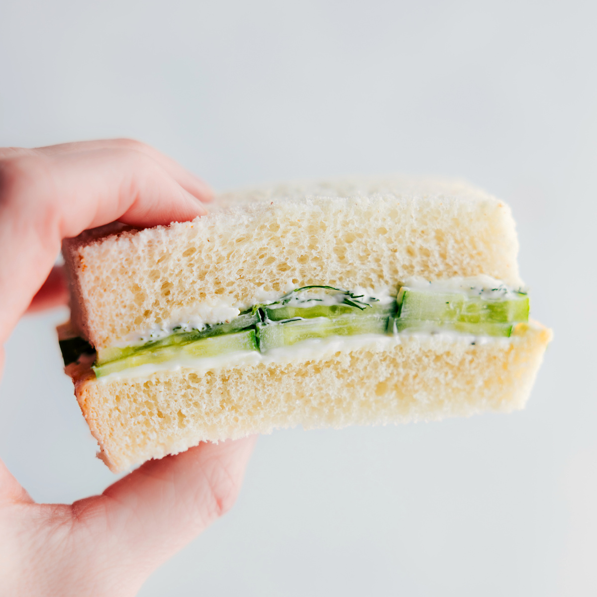 A cucumber sandwich being held up showing the yummy insides.