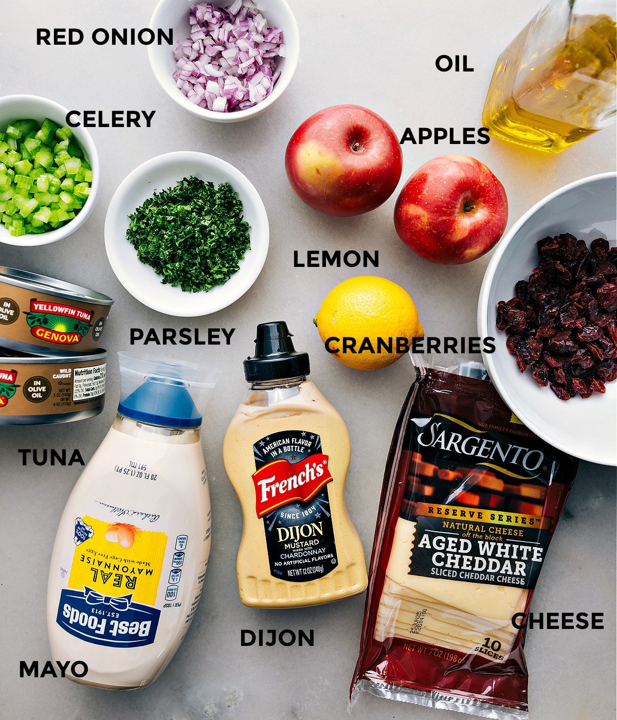 All the ingredients in this recipe are prepped and ready for easy assembly—apples, cranberries, lemon, oil, onion, celery, parsley, cheddar, Dijon, mayo, and meat.