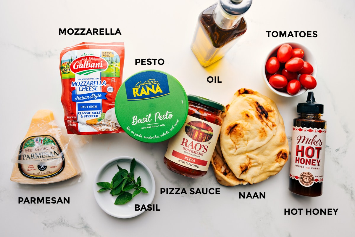 All the ingredients prepped out for easy assembly including the parmesan, mozzarella, pesto, basil, sauce, oil, naan, hot honey, and tomatoes.