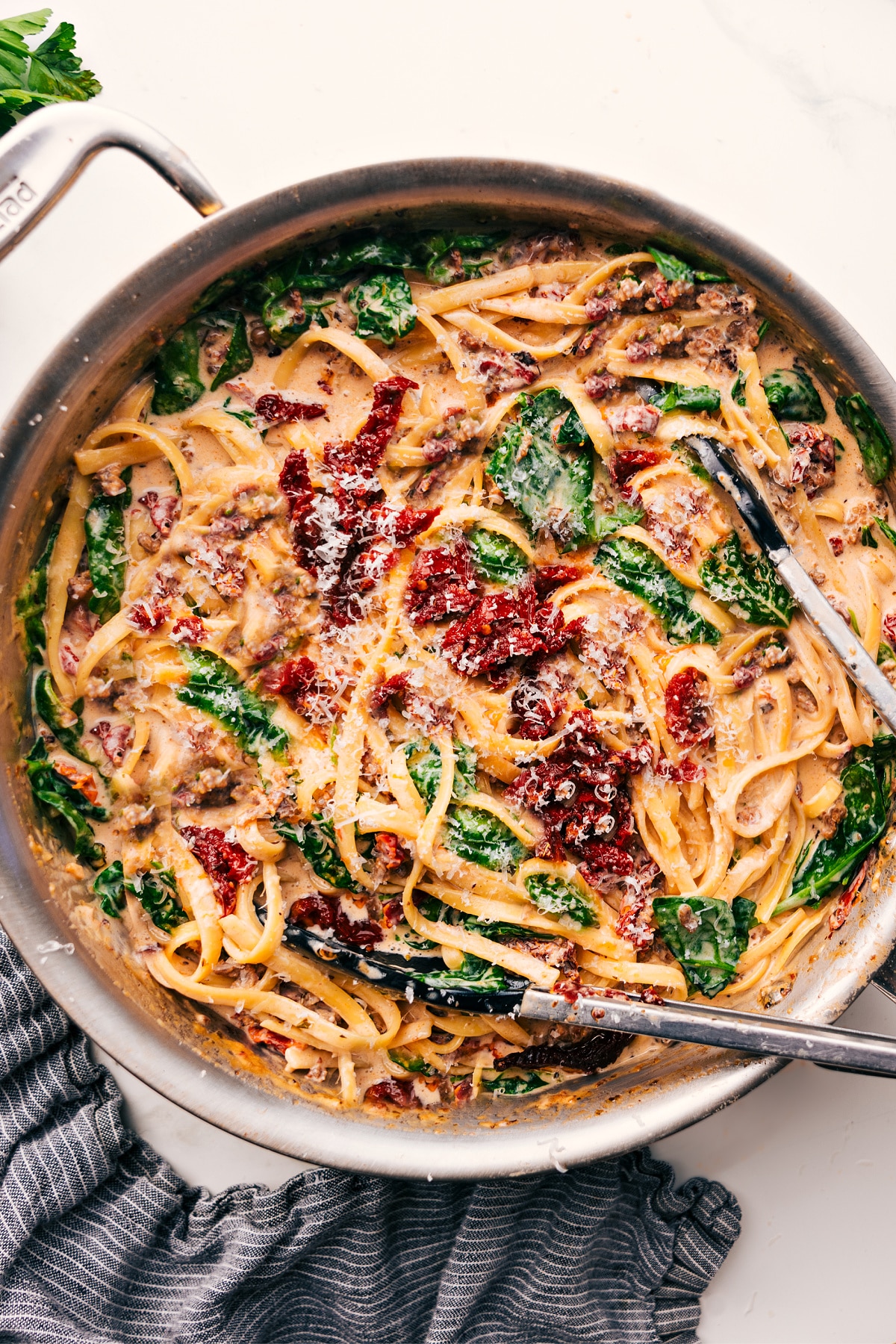 Creamy Sausage Pasta starts with thick, saucy fettuccine tossed with crumbled Italian sausage, succulent sun-dried tomatoes, and tender spinach. Recipe via ChelseasMessyApron #dinner #quick #easy #simple #best #spinach #fettuccine #creamy #sausage #pasta Creamy sausage pasta in a pot, ready to serve.