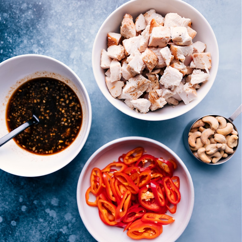 Chicken, cashews, sliced peppers, and a sauce laid out for assembly. 