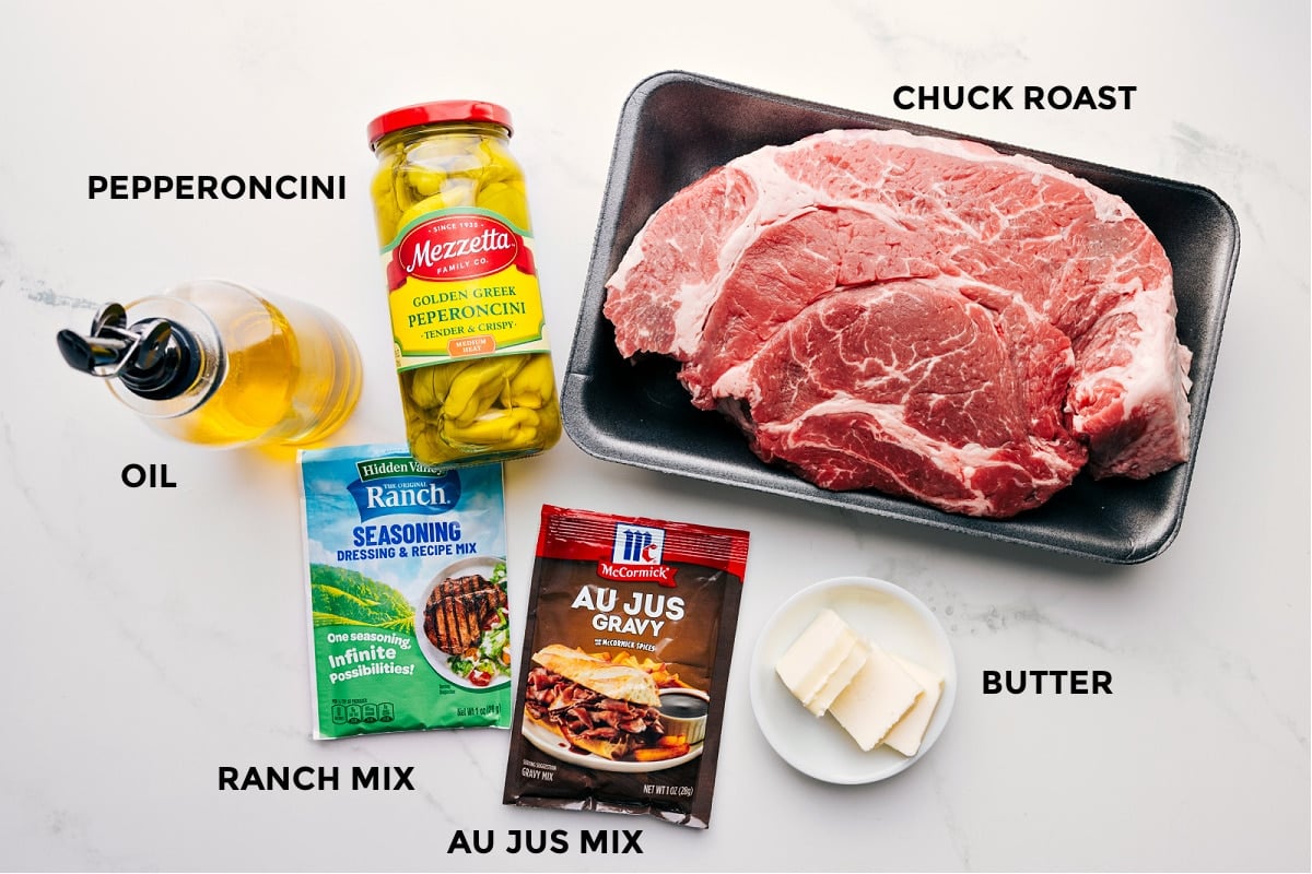 Ingredients prepped for easy assembly: pepperoncini, chuck roast, ranch mix, au jus mix, butter, and oil.