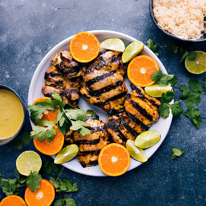 Overhead view of citrus marinated chicken, with cut oranges and limes on the side.