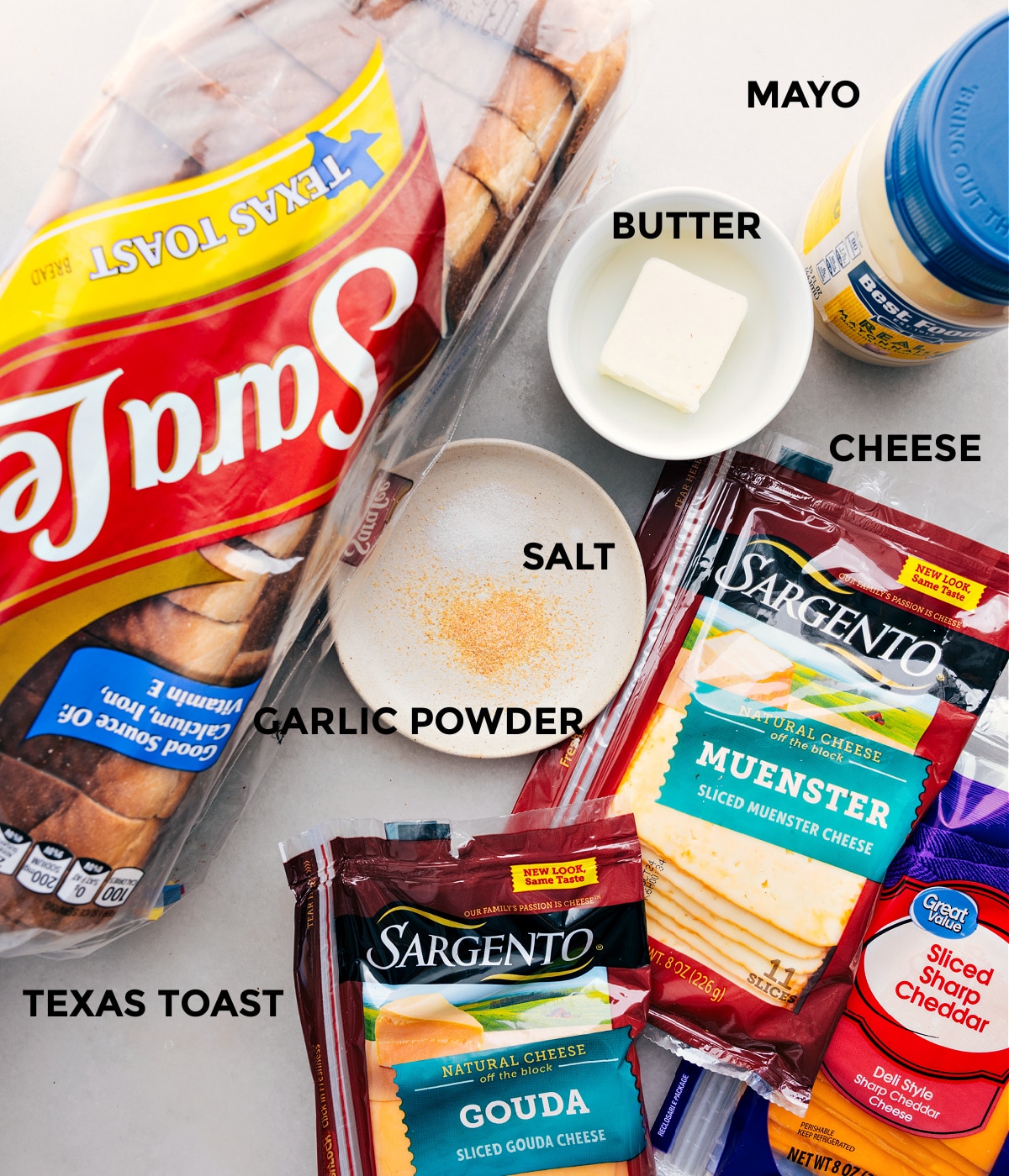All the ingredients in this recipe prepped out for easy assembly including bread, cheddar, muenster, gouda, mayo, butter, and seasonings.