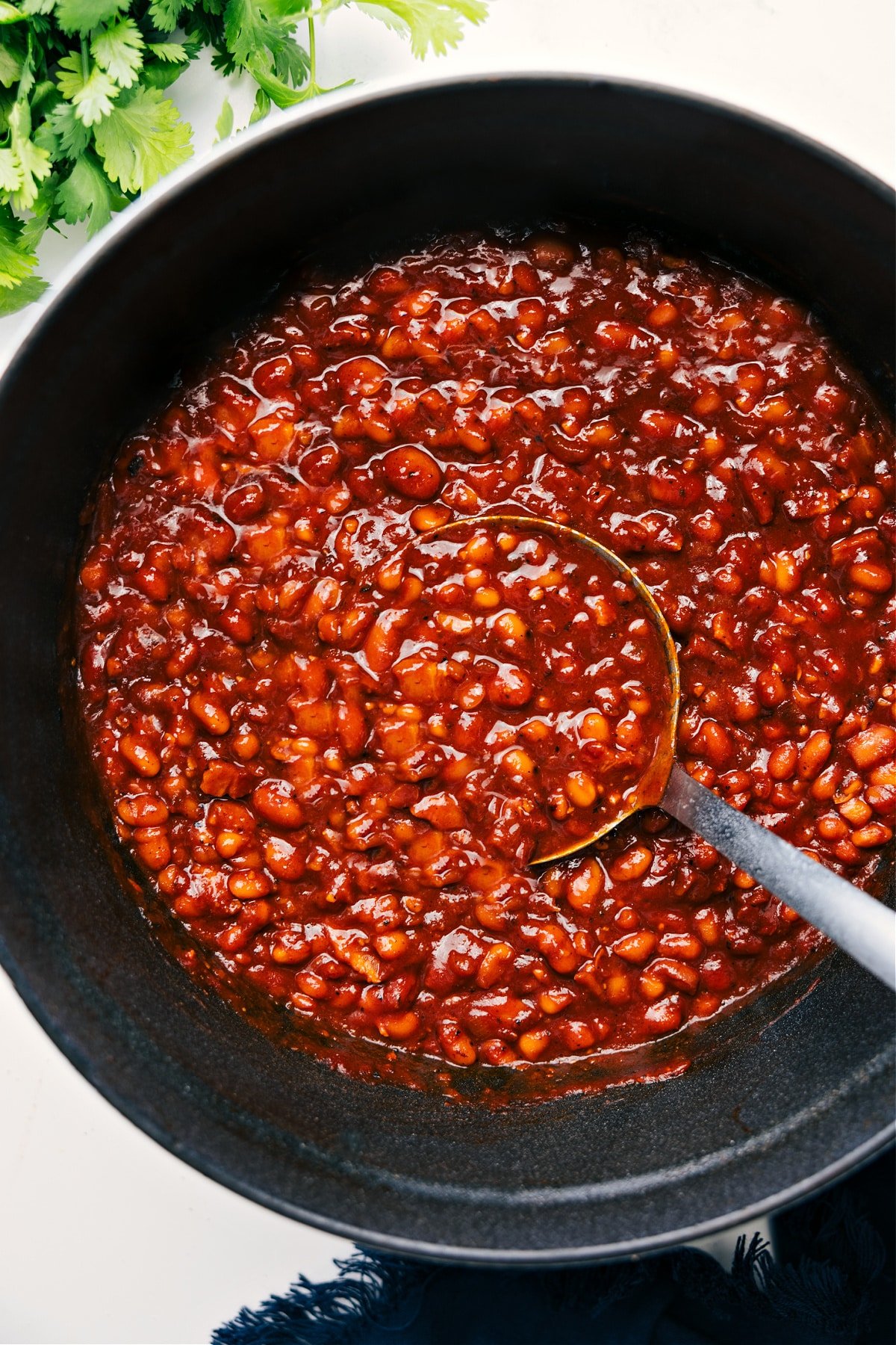 The Best Side: Baked Bean Recipe Baked Beans in a pot with a ladle lifting a hearty scoop.