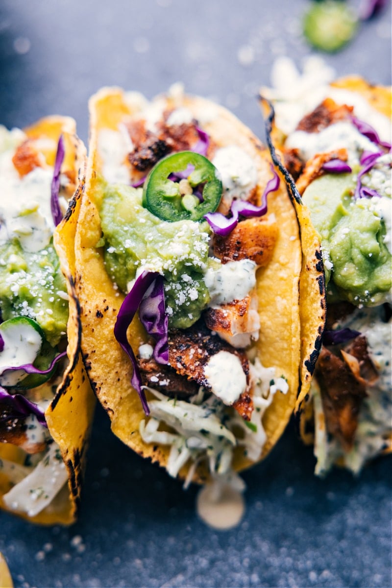 Tasty Tilapia Fish Tacos start with charred corn tortillas and are loaded with a saucy cilantro-lime slaw, taco-seasoned Tilapia, and a scoop of guacamole. These tacos are light, flavorful, and packed with good-for-you ingredients! Recipe via ChelseasMessyApron #dinner #quick #easy #simple #best #fresh #clean #cleaneating #familyfriendly #kidfriendly #tilapia #fish #tacos Overhead image of Tilapia Fish Tacos