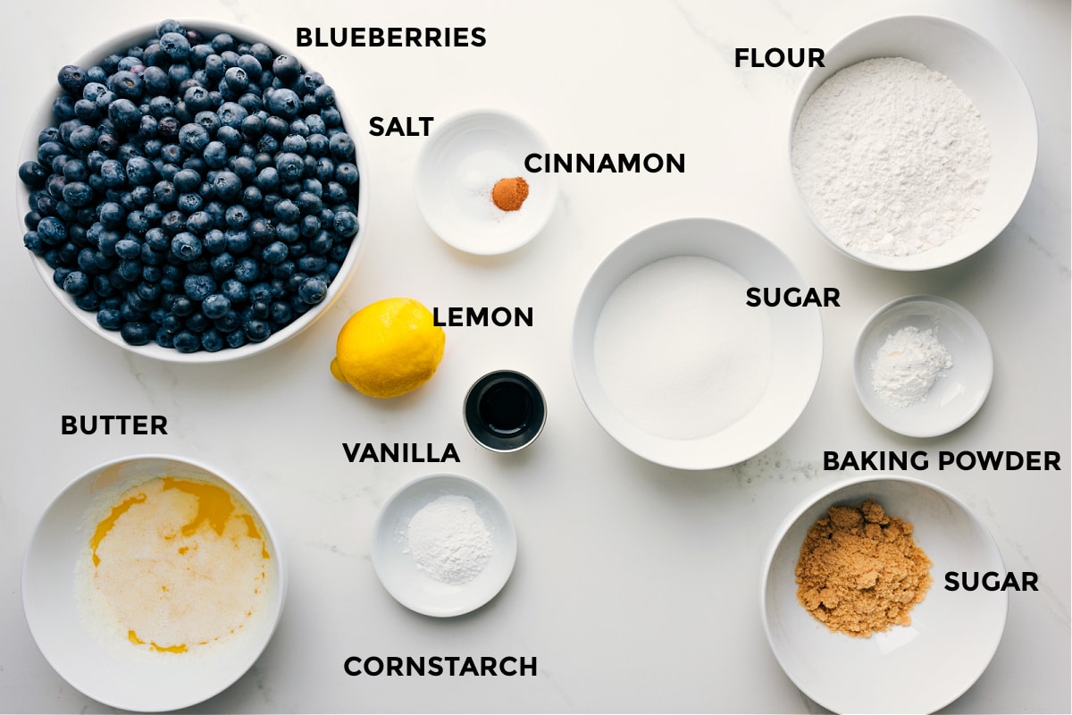 All the ingredients prepped for easy assembly: blueberries, salt, cinnamon, flour, sugar, baking powder, cornstarch, lemon, vanilla, and butter.