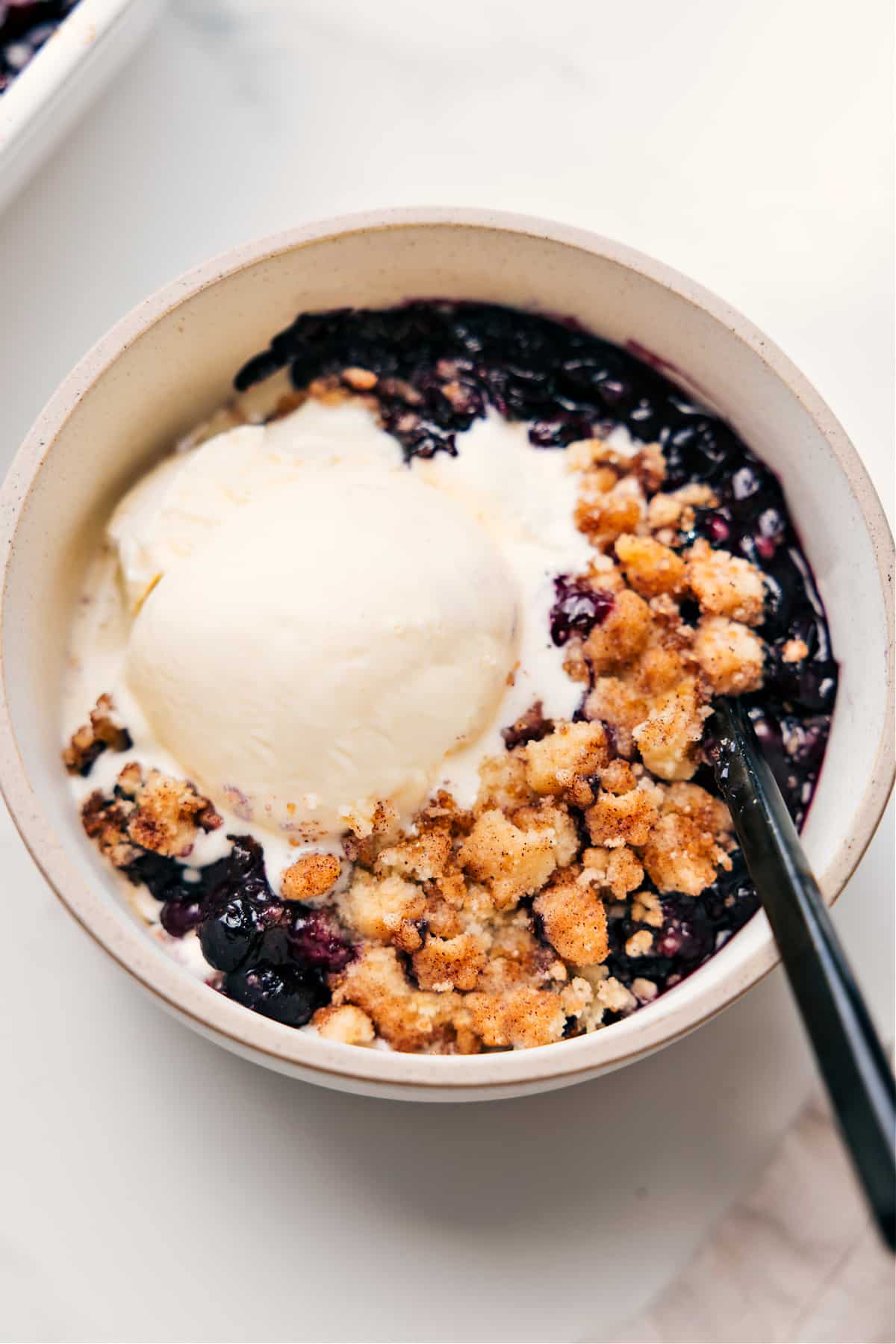 Absolutely The Best Blueberry Cobbler Recipe Blueberry Cobbler Recipe served in a bowl with a scoop of vanilla ice cream on top.