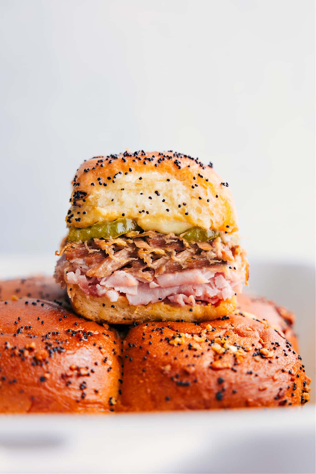 The Best Cuban Sliders Recipe Cuban Sliders stacked on top of each-other showing the delicious layers of meat and pickles.