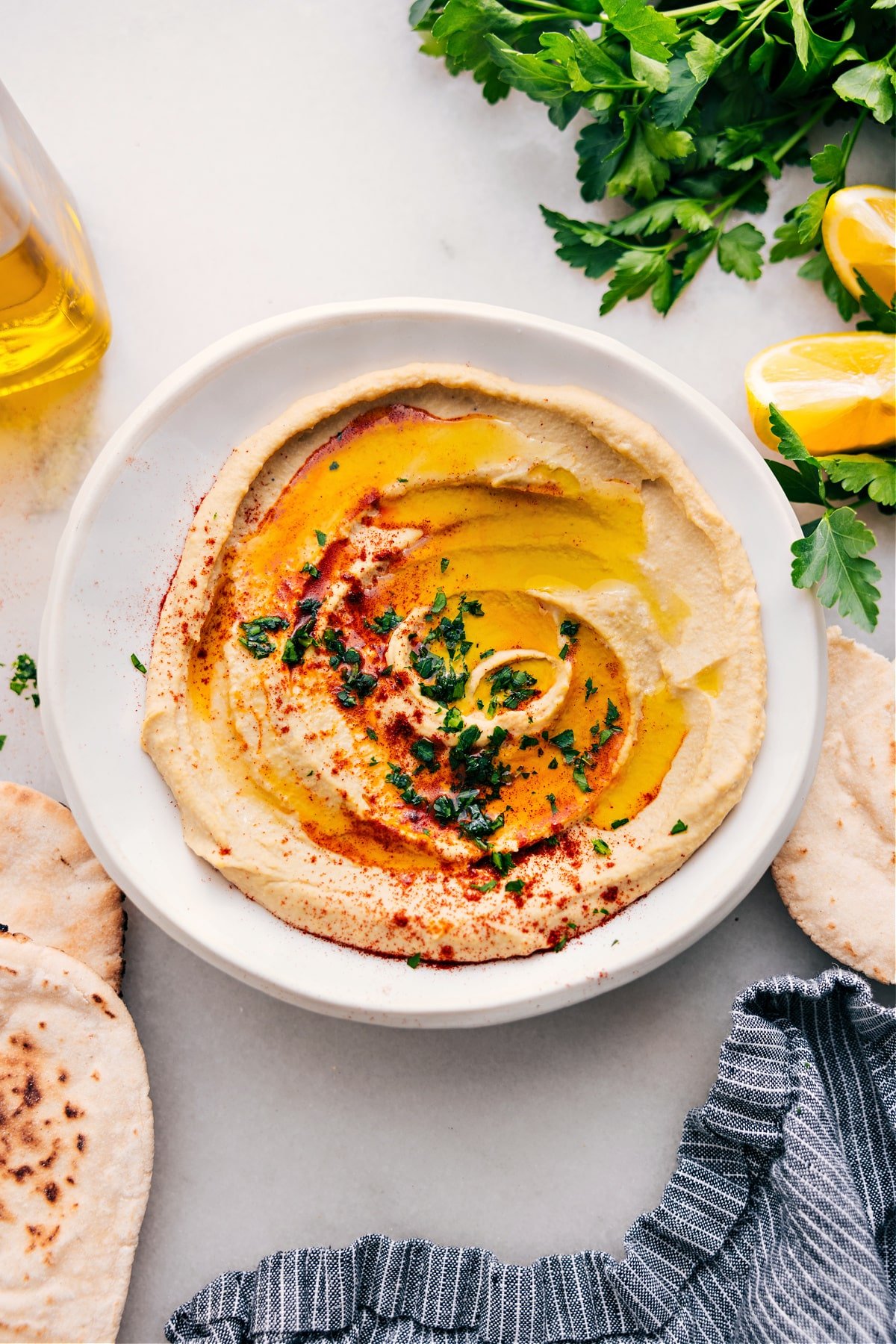 Middle Eastern Hummus Recipe Hummus in a bowl with fresh olive oil, herbs, and paprika on top.