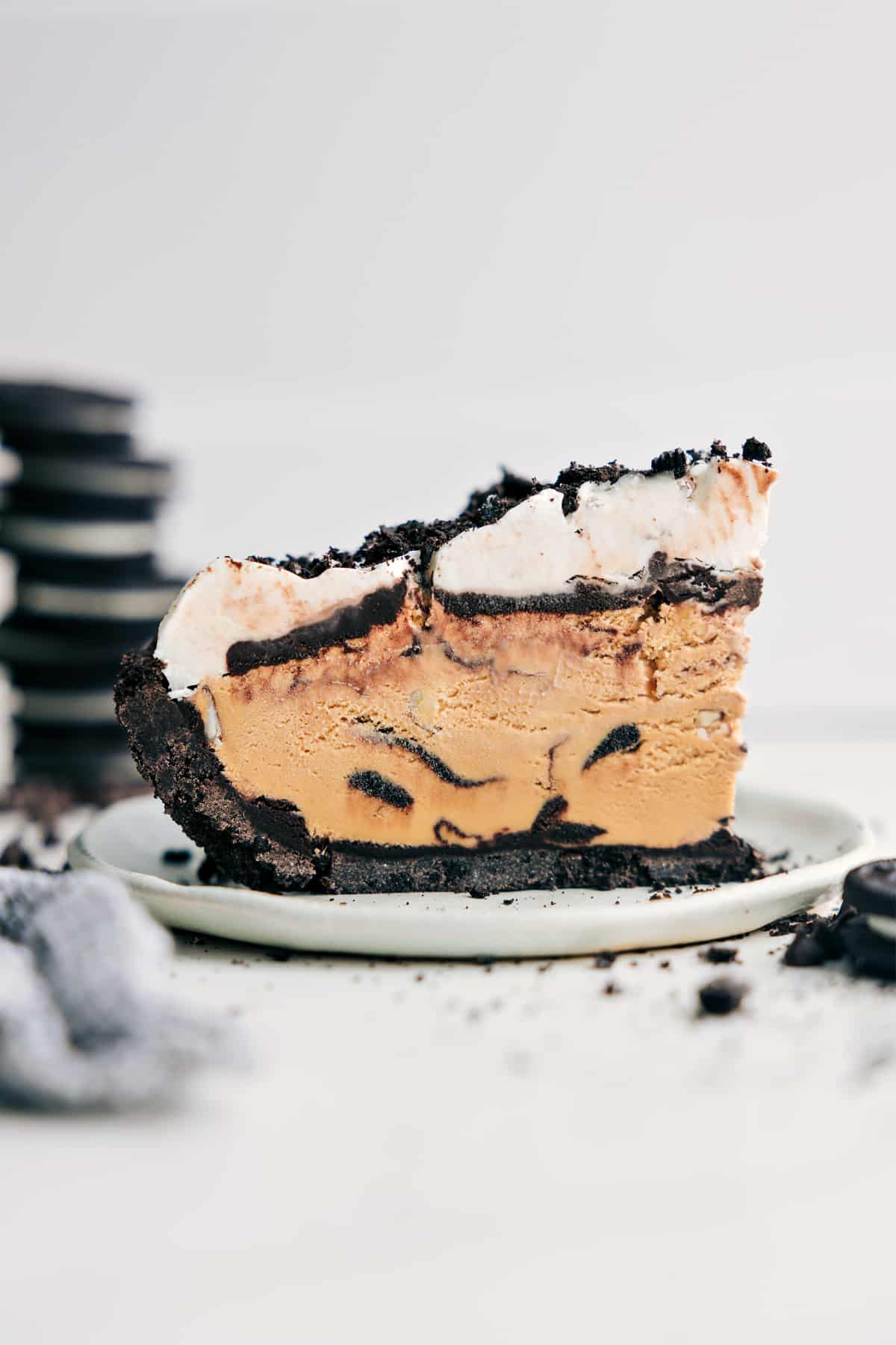 Mississippi Mud Pie is such a favorite for kids and adults alike! We start with a sweet Oreo cookie crust that is topped with hot fudge, coffee-flavored (or chocolate) ice cream, one more layer of fudge, and then creamy whipped topping to finish things off. Recipe via ChelseasMessyApron #dessert #best #quick #easy #simple #treat #quick #nobake #crust #familyfriendly #kidfriendly #mississippi #mud #pie A slice of this Mud Pie Recipe on a plate, showing off all the delicious layers.