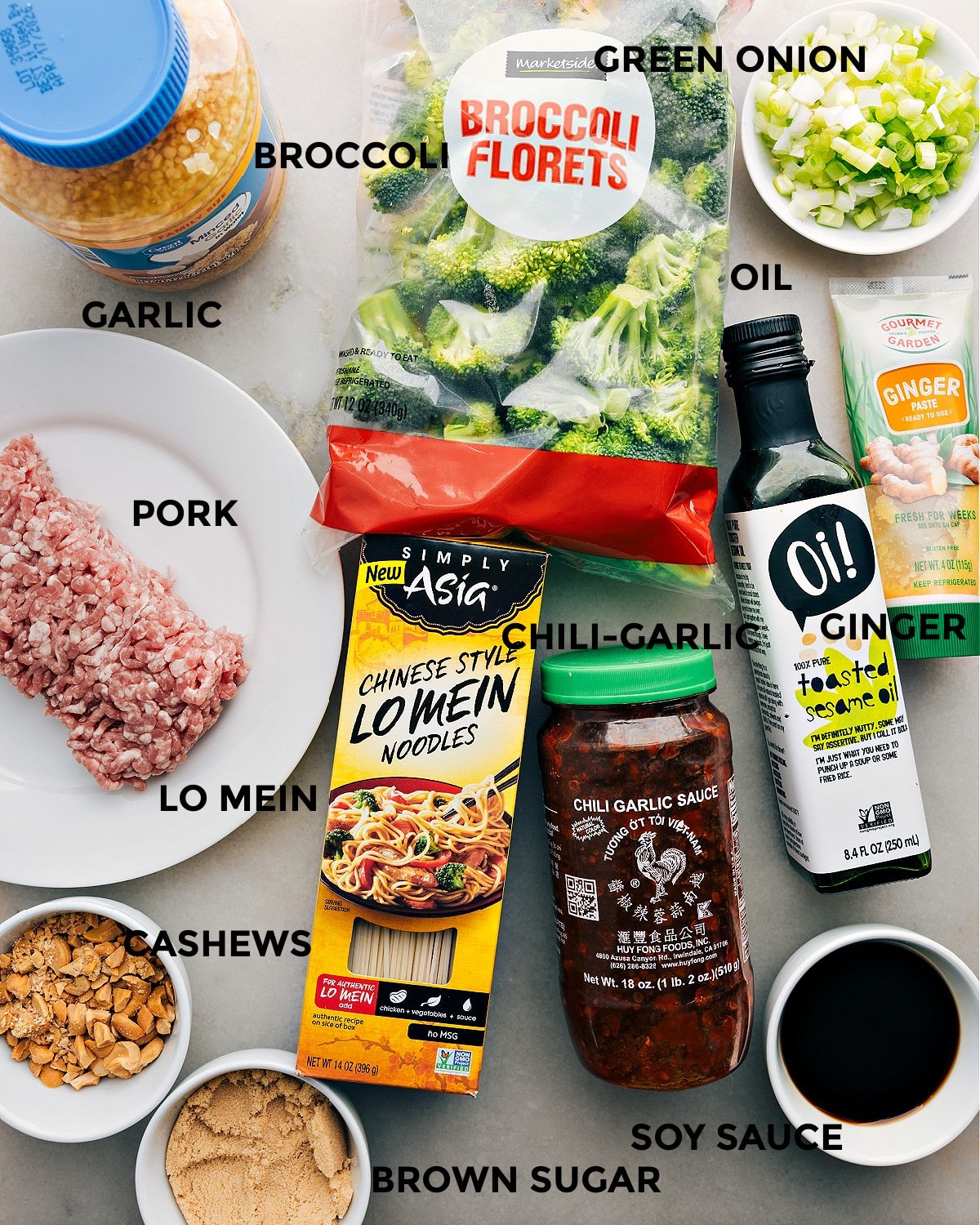 All the ingredients in this recipe including pork, broccoli, green onions, noodles, chili garlic sauce, ginger, soy sauce, brown sugar, cashews, and garlic prepped out for easy assembly.