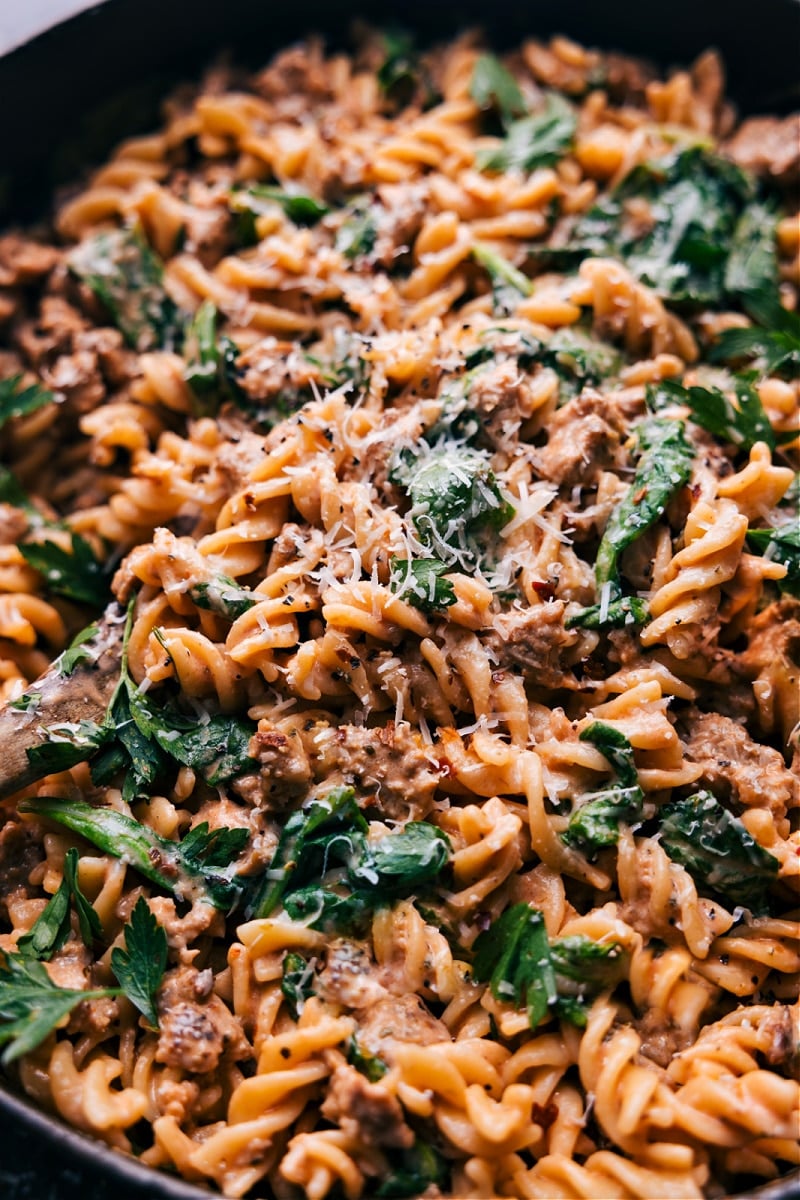 Sausage Pasta is the ultimate comfort food! Italian sausage in a creamy tomato sauce with fresh baby spinach and tender pasta. Topped with some freshly grated Parmesan cheese--this dish is unbelievably good! Recipe via chelseasmessyapron #dinner #quick #easy #simple #best #familyfriendly #kidfriendly #comfortfood #cheesy #sausage #pasta Overhead image of the sausage pasta