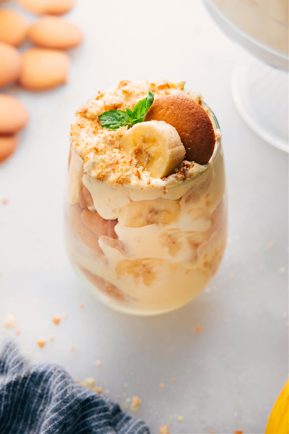 A glass filled with layers of the delicious banana pudding recipe, alternating between pudding, vanilla cookies, fresh bananas, and topped with vanilla cookie crumbs, creating a delightful dessert.