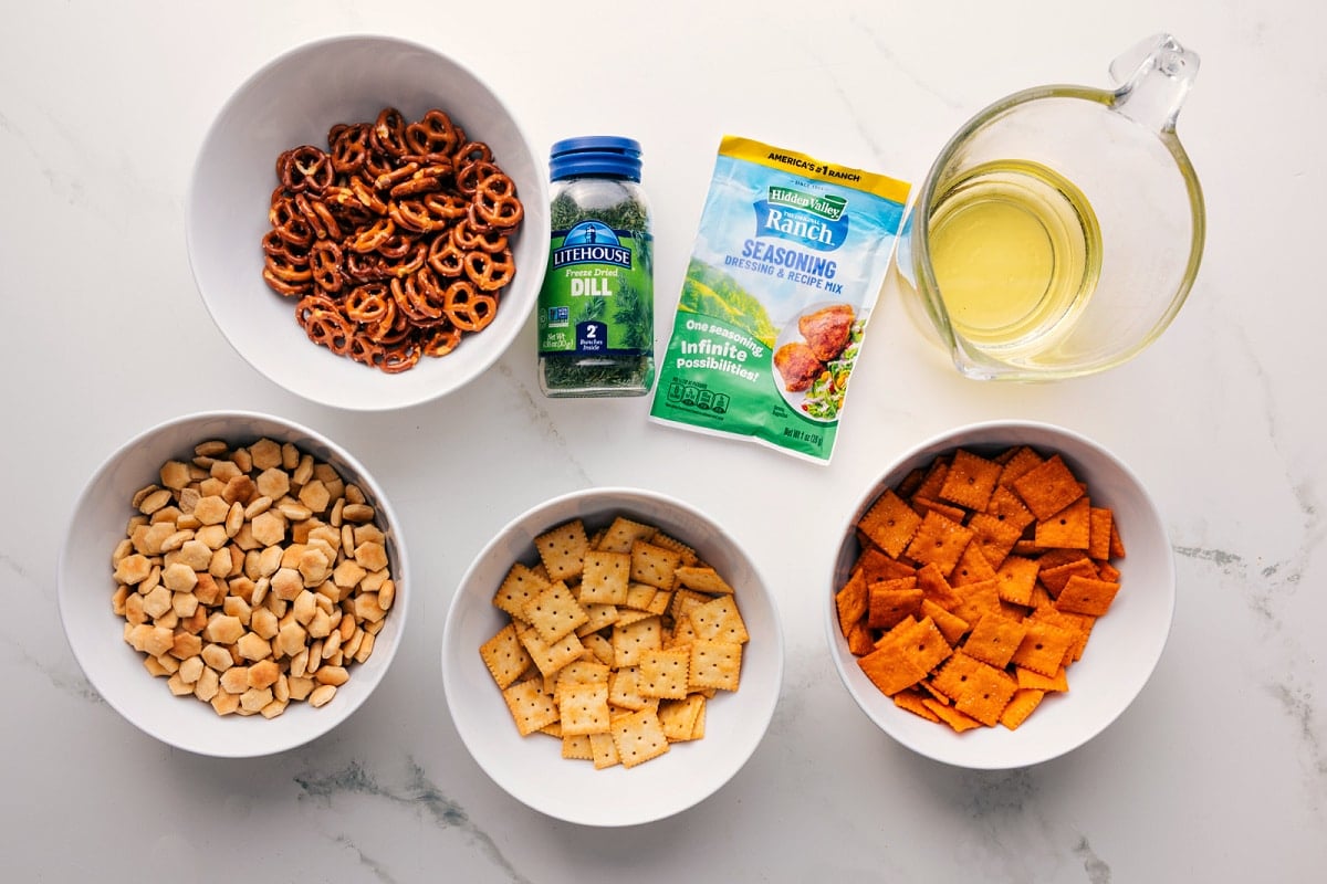 This Chex Mix Recipe is loaded with crispy cereal, pretzels, cheese crackers, and nuts. The seasoned butter pulls everything together into a mix that is nothing short of addicting! Recipe via ChelseasMessyApron.com #snackmix #chexmix #chex #snack #cereal All the ingredients in this recipe prepped out for easy assembly including the pretzels, crackers, seasonings, dill, and oil.