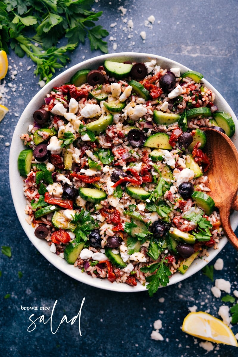 Looking for a tasty and healthy Mediterranean-inspired dish? Try this Brown Rice Salad! This recipe brings together the nutty flavor of brown rice with the fresh and vibrant flavors of the Mediterranean. It's filled with crisp cucumbers, roasted red peppers, sun-dried tomatoes, red onion, parsley, and crumbled feta cheese, all tossed in a flavorful lemon dressing. Recipe via chelseasmessyapron #sidedish #best #quick #easy #simple #familyfriendly #kidfriendly #cucumber #sundriedtomatoes #brownrice #salad Overhead image of Brown Rice Salad