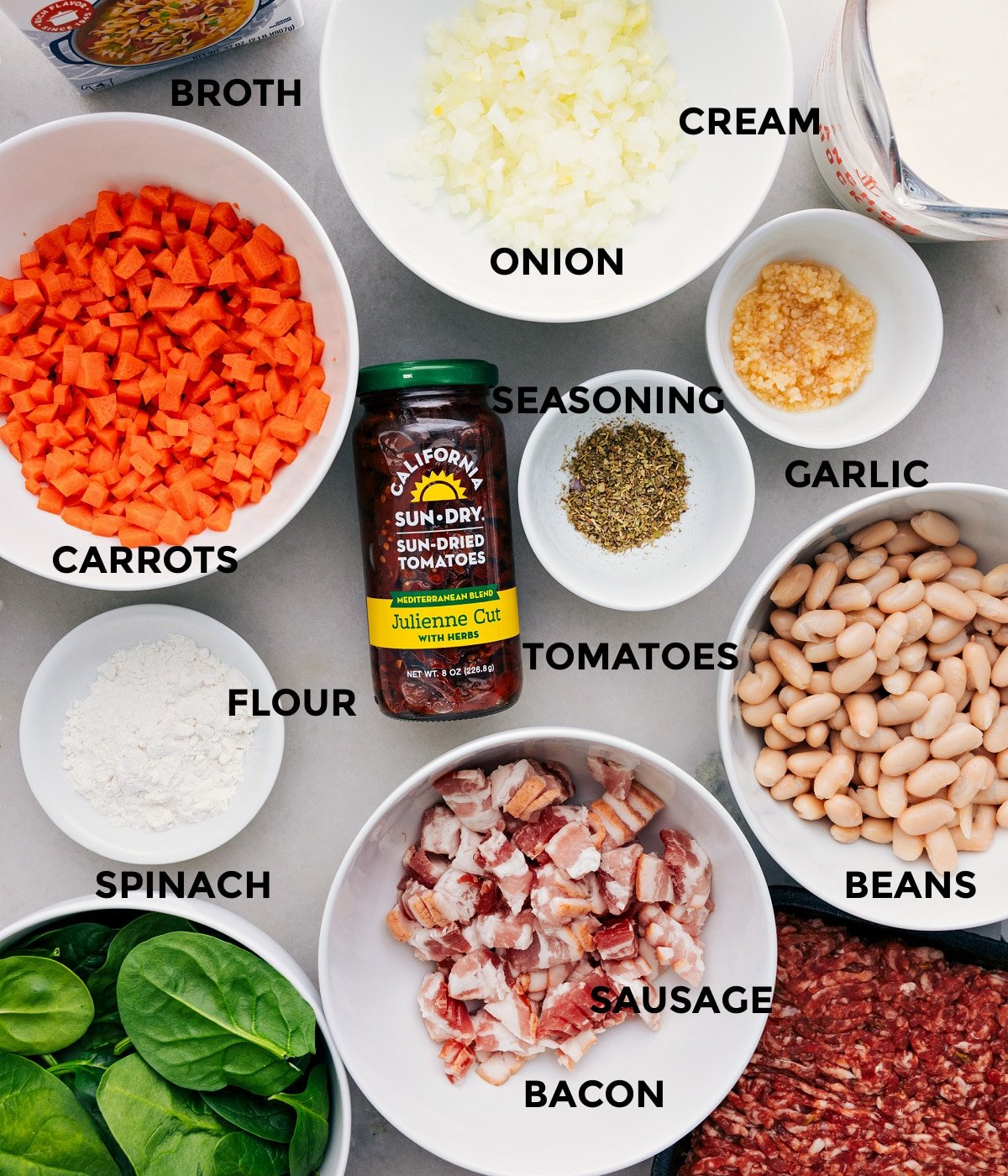 All the ingredients in this recipe—veggies, seasoning, tomatoes, beans, sausage, bacon, spinach, flour, broth, and cream.