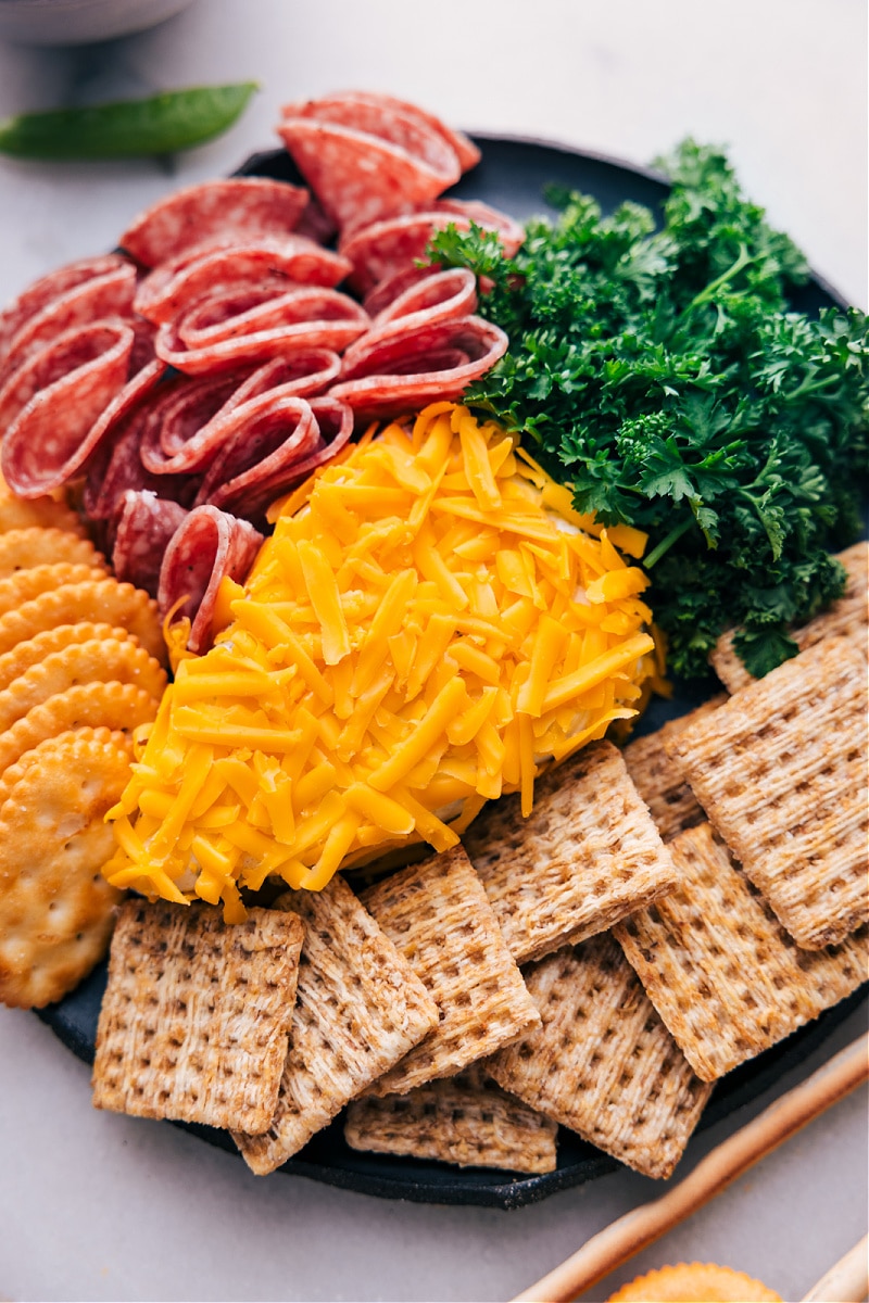 Imagine this: you're hosting a gathering, and you want to serve a fun, eye-catching appetizer that will not only impress your guests but also taste amazing. Look no further than this fun "Carrot" Cheeseball recipe! This creation combines the creamy goodness of Boursin cheese with the sharp, savory flavor of Cheddar cheese, all shaped to resemble a carrot! It's a perfect conversation starter and a tasty treat that pairs beautifully with an array of crackers, cold cuts, and fresh veggies. Recipe via chelseasmessyapron #sidedish #best #quick #easy #appetizer #snack #easter #spring #snackboard #carrot #cheeseball Overhead image of the Carrot Cheeseball