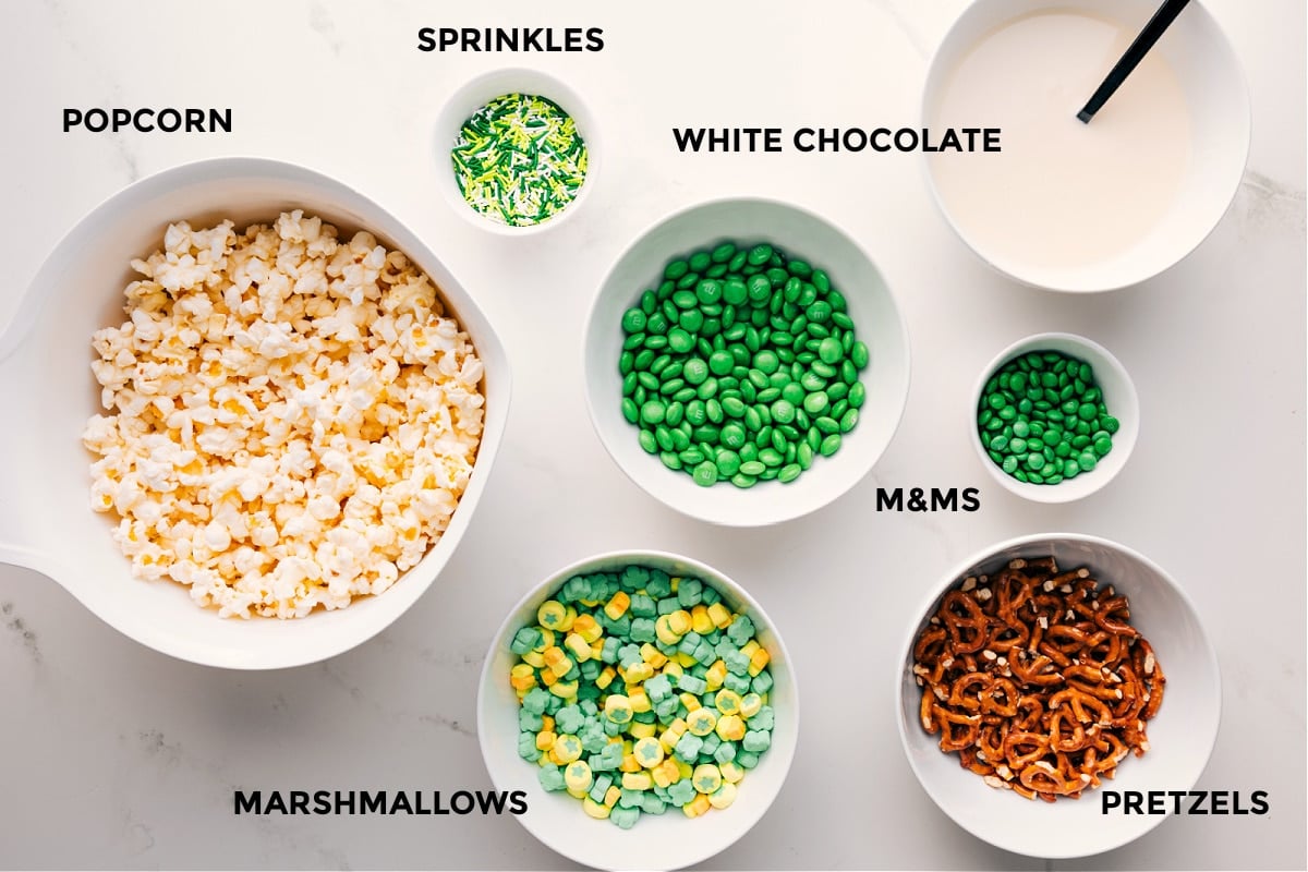 Ingredients In St. Patrick's Day Popcorn All the ingredients for this recipe prepped out for easy assembly including the popcorn, sprinkles, marshmallows, M&Ms, white chocolate, and pretzels.