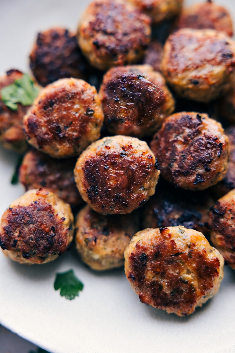 Chicken meatballs are a tasty and nutritious alternative to traditional beef and pork meatballs. Packed with flavor and easy to make, they're the perfect weeknight dinner option. Plus, there's no need to slave over browning meatballs on the stovetop—these meatballs are baked all at once! Serve them with our favorite pesto pasta for a delicious and satisfying meal that will become a new family favorite! Recipe via chelseasmesssyapron #dinner #quick #easy #simple #familyfriendly #cleaneating #protein #chicken #meatballs Overhead image of Chicken Meatballs on a plate ready to be enjoyed