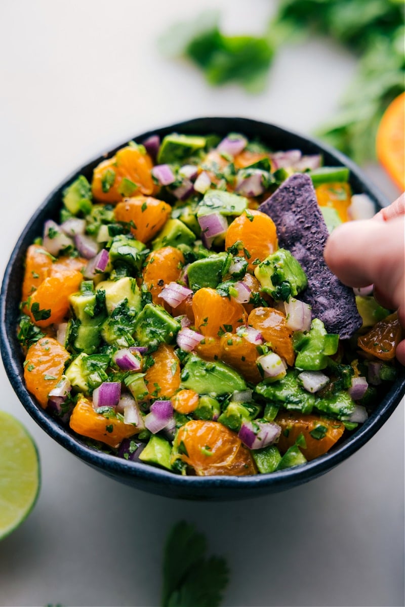 The Avocado-Orange Salsa is a vibrant and refreshing recipe that combines the creamy richness of avocados with the tangy sweetness of mandarin oranges. It's a perfect blend of flavors and textures that can be enjoyed as a dip or a topping for various dishes. Recipe via chelseasmessyapron #healthy #quick #easy #simple #sidedish #chips #dipandchips #summer #bbq #avocado #orange #salsa Overhead image of Avocado-Orange Salsa