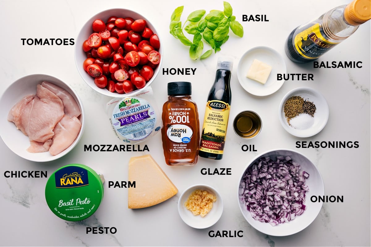 All the ingredients for this recipe are prepped and ready for easy assembly, including basil, meat, balsamic, butter, seasonings, onion, oil, glaze, honey, garlic, Parmesan, mozzarella, pesto, and tomatoes.