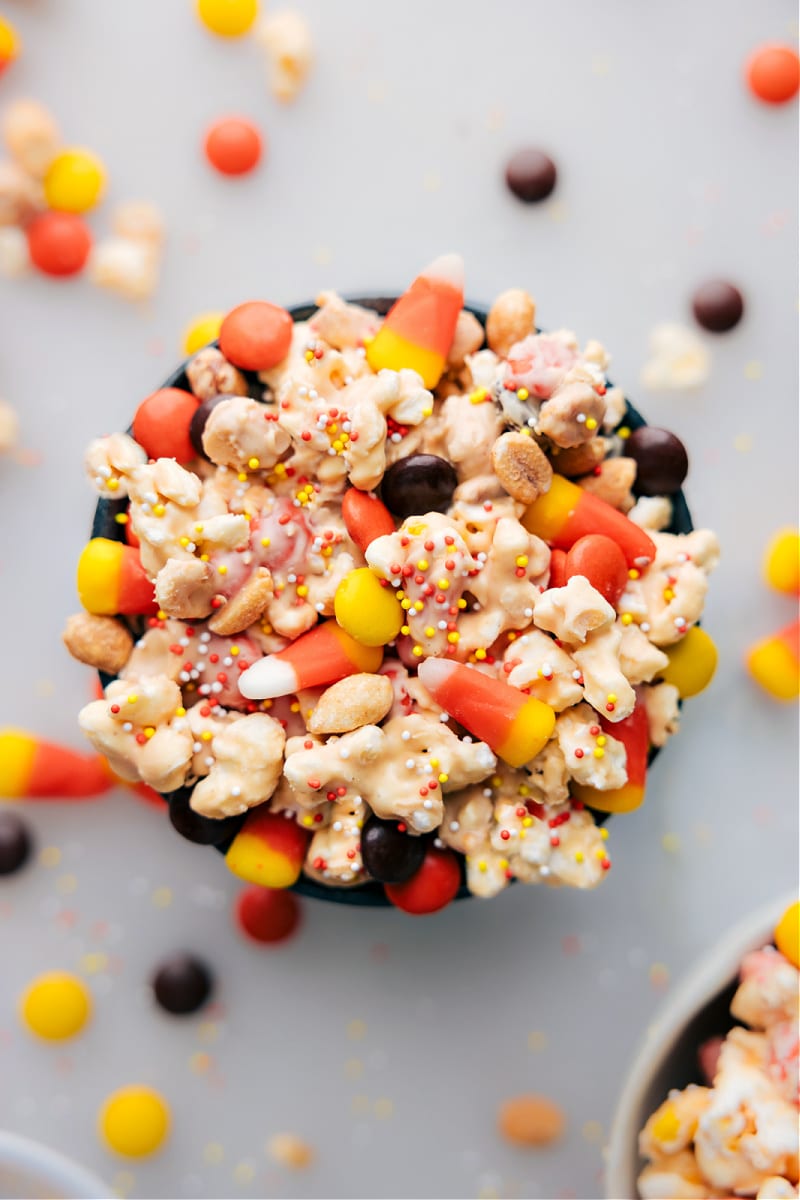 Candy Corn Popcorn is all about giving popcorn a sweet makeover! We coat it in a creamy blend of peanut butter and white chocolate, then throw in candy corn, dry-roasted peanuts, and crunchy peanut candies. This fall snack mix is so addictive, that you'll struggle to stop at just one handful - a guaranteed crowd-pleaser! Recipe via ChelseasMessyApron.com #candycorn #popcorn #whitechocolate #peanutbutter #halloween #treat #kidfavorite Overhead view of Candy Corn Popcorn