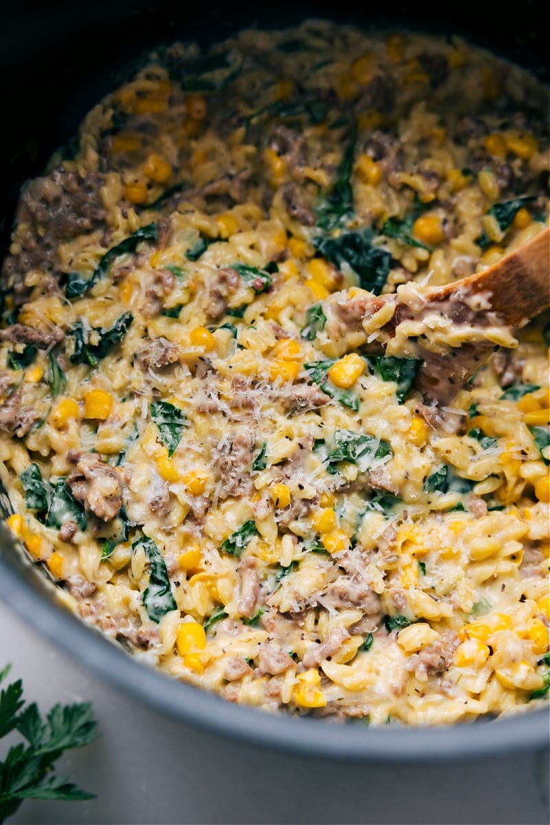 One Pan Sheet Pan Sausage And Potatoes Sausage, corn, and spinach orzo in a pot.