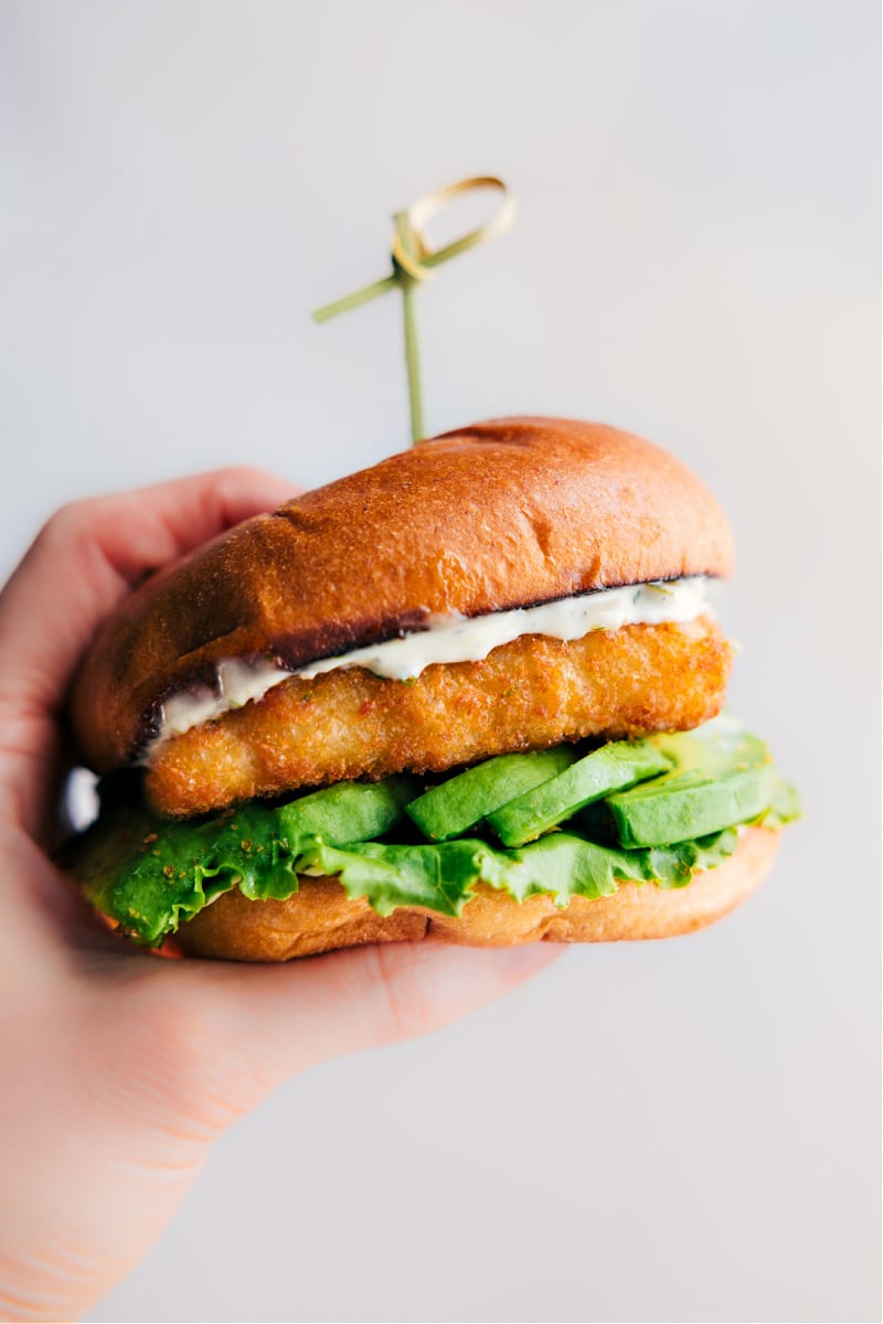 View of a hand holding a fully assembled Fish Sandwich